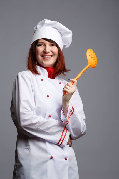 Picture woman cooks in white robe and cap with slotted spoon in hand - Fotó, kép