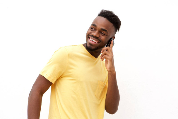 Porträt eines jungen schwarzen Mannes, der vor weißem Hintergrund auf dem Handy lächelt und spricht  - Foto, Bild
