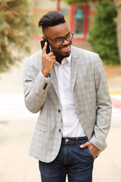 Портрет молодого черного бизнесмена в очках, выходящего на улицу и разговаривающего по мобильному телефону
 - Фото, изображение