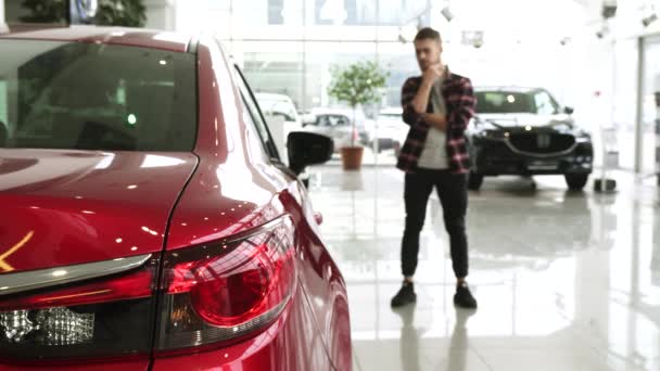 Αρσενικό πελάτη γενειάδα τρίβει σκεπτικά επιλέγοντας ένα νέο αυτοκίνητο στην αντιπροσωπεία - Πλάνα, βίντεο