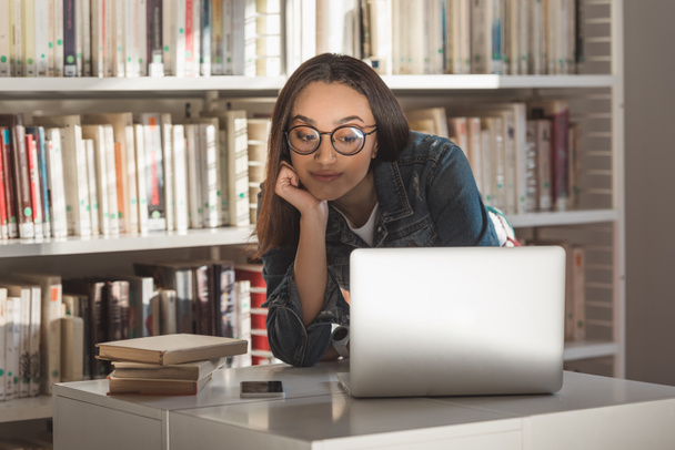 Afryki amerykański dziewczyna patrząc na laptopie w bibliotece - Zdjęcie, obraz