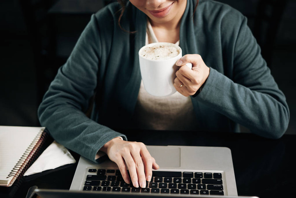 Immagine ritagliata di studentessa che beve caffè e lavora sul computer portatile
 - Foto, immagini