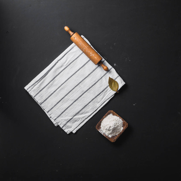deegroller en meel met servet op zwarte achtergrond - Foto, afbeelding