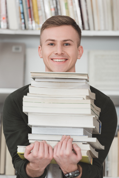 estudiante sonriente sosteniendo pila de libros y mirando a la cámara
 - Foto, Imagen