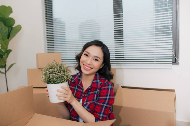 Portrait de femme heureuse déménageant dans une nouvelle maison tenant la plante verte en pot
 - Photo, image