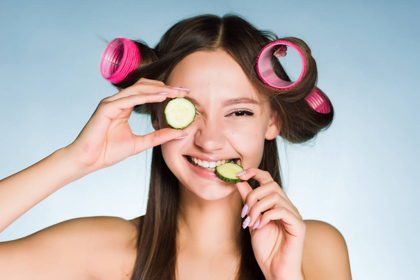 Gelukkige vrouw met krulspelden op haar hoofd eten komkommer - Foto, afbeelding