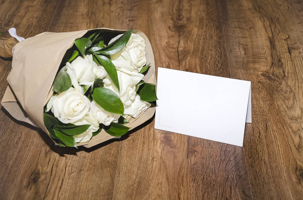 красивый букет белых роз в крафтовой бумаге и белый лист бумаги на деревянном фоне
 - Фото, изображение