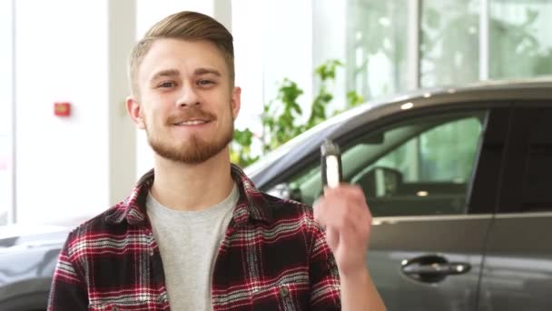 attraktiver junger Mann lächelt und posiert mit Autoschlüsseln im Autohaus - Filmmaterial, Video