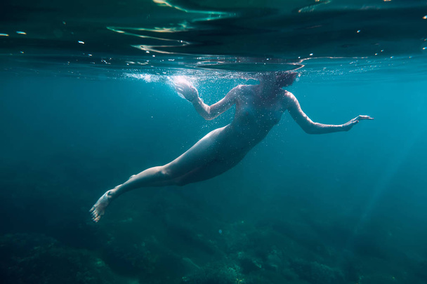 Naked young woman swimming underwater in blue ocean - Фото, зображення