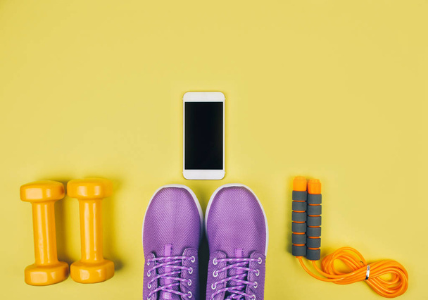 Flat lay shot of sneakers, dumbbells, jump rope or skipping rope and smartphone. - Фото, изображение