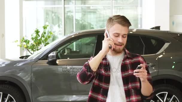 Szczęśliwy młody człowiek rozmawia przez telefon po zakupie nowego samochodu w dealrrship - Materiał filmowy, wideo