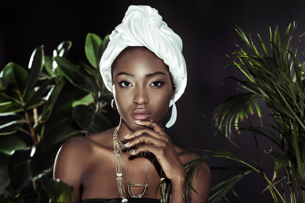young african american woman in white wire head wrap behind leaves looking at camera - Foto, Bild