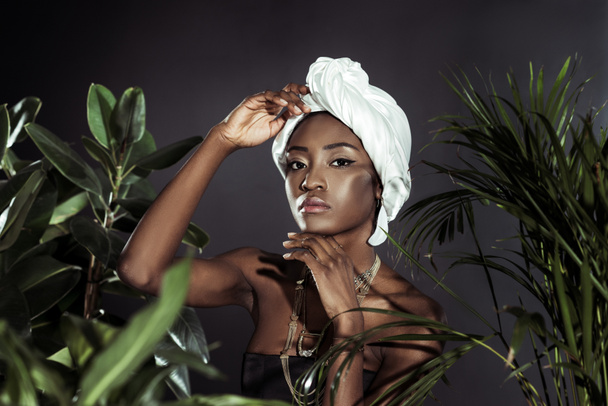 fashionable african american woman in white wire head wrap behind leaves - Foto, Bild
