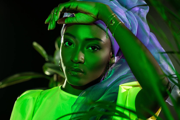 piękne african american Kobieta w tradycyjne drutu owinąć głowę pod zielone światło za liści - Zdjęcie, obraz