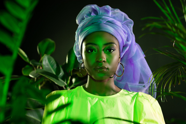 young african american woman in traditional wire head wrap under green light looking at camera - Photo, Image