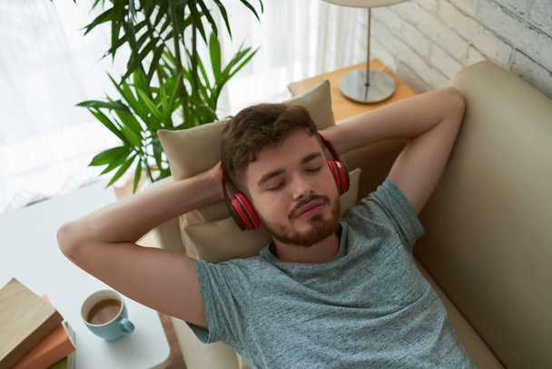 Student relaxing on sofa with music in headphones - Fotó, kép