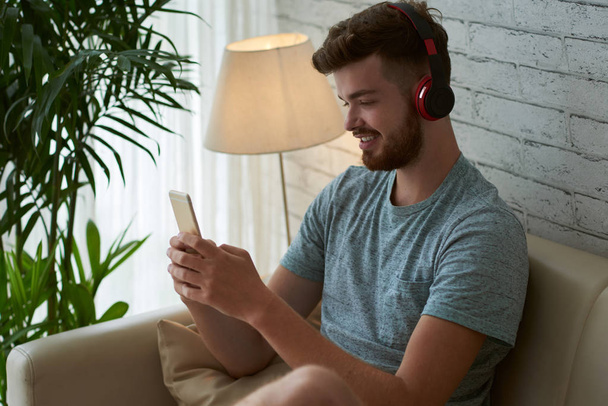 Vrolijke jongeman, luisteren naar muziek en SMS met vrienden in mobiele telefoon - Foto, afbeelding