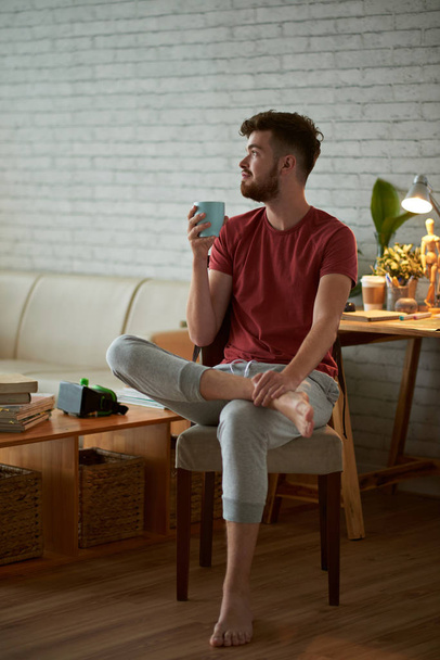 若い男の椅子に座って、新鮮なコーヒーのカップを飲む - 写真・画像