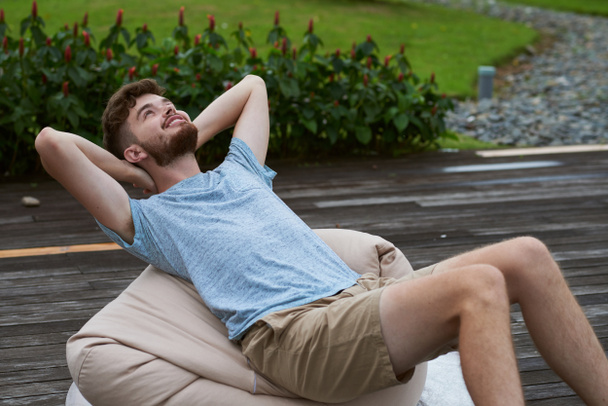 Hombre joven relajándose en la silla de frijol al aire libre
 - Foto, Imagen