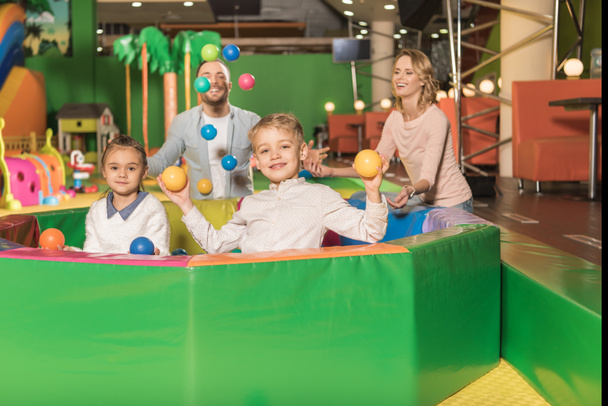 happy parents looking at cute little kids smiling at camera and playing with colorful balls in game center - Fotografie, Obrázek