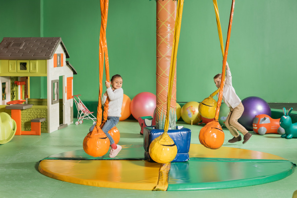 fröhliche kleine Kinder schaukeln und spielen im Unterhaltungszentrum - Foto, Bild