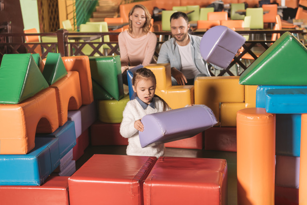 happy parents looking at little daughter building castle with colorful blocks in game center - Φωτογραφία, εικόνα