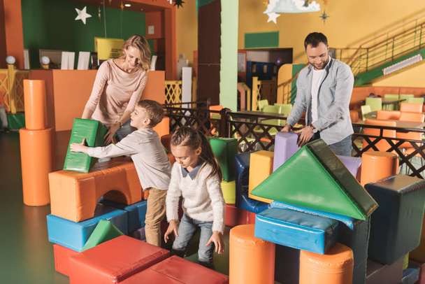 onnellinen perhe, jossa kaksi lasta leikkii värikkäillä lohkoilla pelikeskuksessa
  - Valokuva, kuva