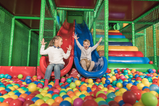 adorables niños felices deslizándose en la piscina con bolas de colores
 - Foto, imagen