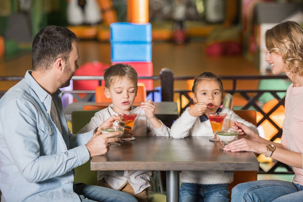 счастливая семья с двумя детьми едят десерты в кафе
 - Фото, изображение