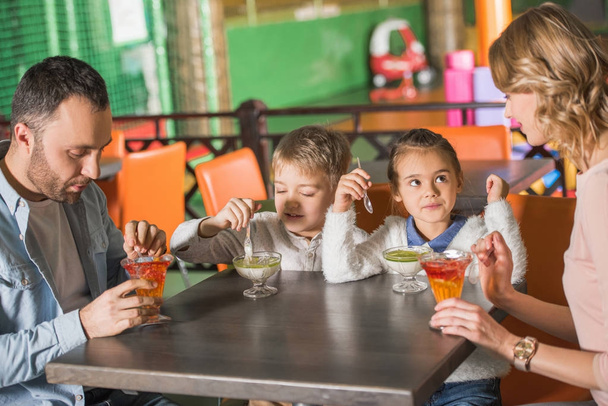 familia con dos niños comiendo sabrosos postres en la cafetería en el centro de entretenimiento
   - Foto, Imagen