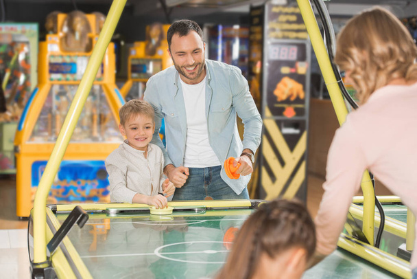 счастливая семья с двумя детьми играть в воздушный хоккей вместе в развлекательном центре
    - Фото, изображение