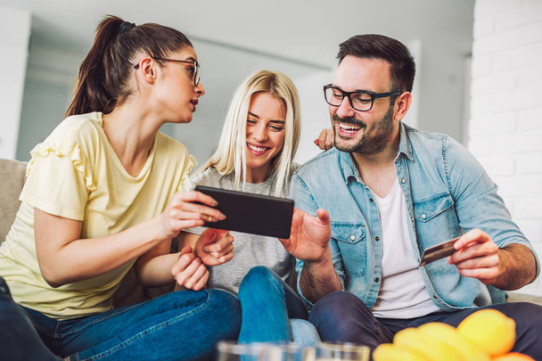 Two women and a man in living room holding credit card and digital tablet - Foto, immagini