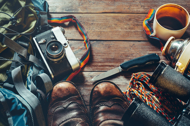 Аксессуары для путешествий на деревянном фоне, вид сверху. Старые сапоги, рюкзак, винтажная пленка и нож
 - Фото, изображение