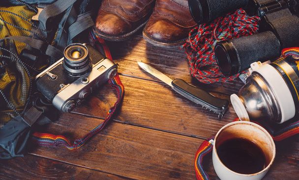 Travel Accessories On Wooden Background. Old hiking leather boots, backpack, vintage film camera, knife and thermos - Foto, immagini
