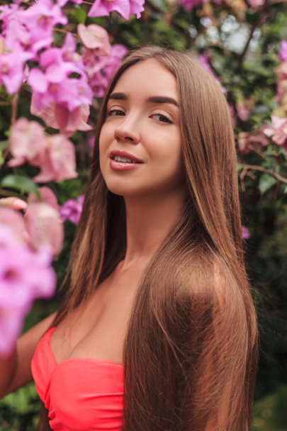 portrait of beautiful young girl posing at pink flowers - Photo, Image
