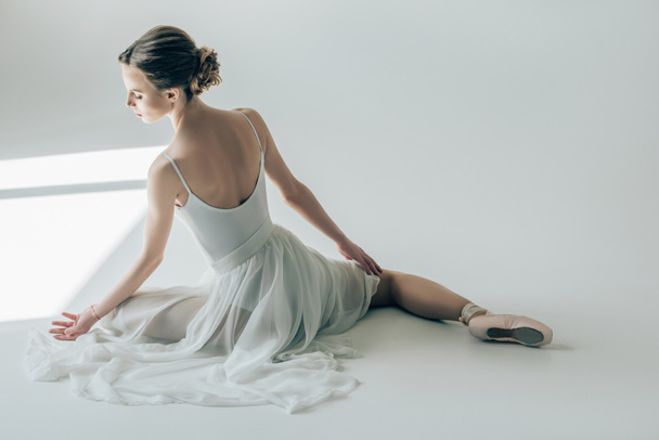 вид сзади балерины, сидящей в белом платье и балетной обуви
 - Фото, изображение
