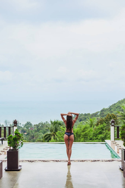 rear view of girl posing at swimming pool on tropical resort - Photo, Image