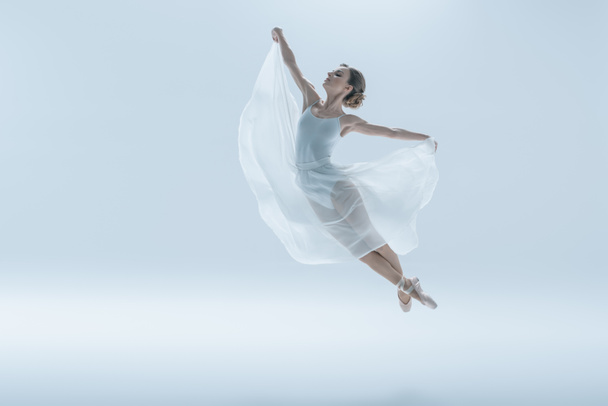 elegant ballet dancer in white dress jumping in studio, isolated on white - 写真・画像