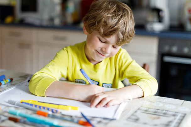 Niño cansado en casa haciendo deberes escribiendo cartas con bolígrafos coloridos
 - Foto, imagen