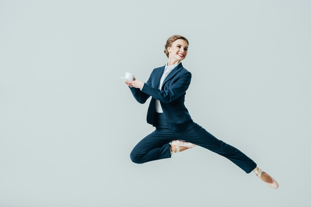 donna d'affari in giacca e cravatta e scarpe da ballo che salta con una tazza di caffè, isolata su grigio
 - Foto, immagini