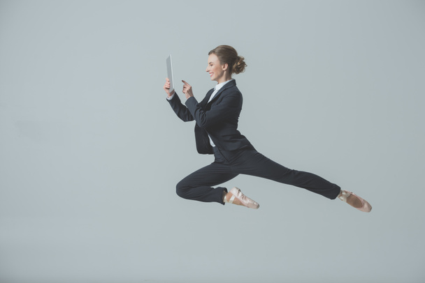 бізнес-леді в костюмі і балеті стрибає і використовує цифровий планшет, ізольовані на сірому
 - Фото, зображення