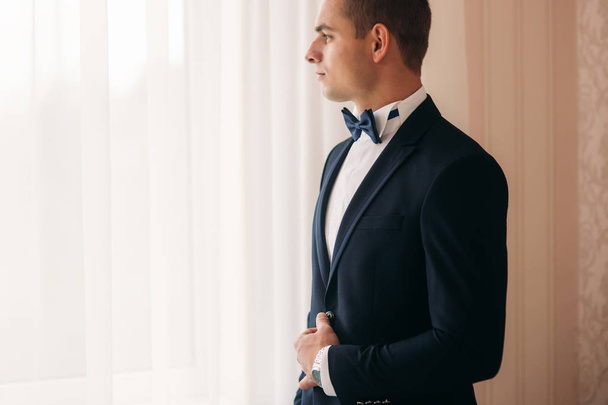 The groom is dressed at home in a suit. Cute groom posing for a photographer - Photo, Image