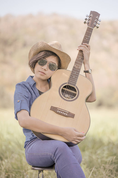 Donne capelli corti indossare cappello e occhiali da sole sedersi a suonare la chitarra in g
 - Foto, immagini