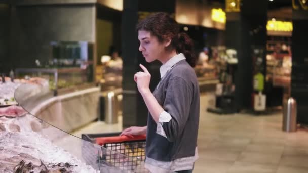 Joven cliente femenina tratando de elegir mariscos en un supermercado. Caminar a lo largo de la fila
 - Metraje, vídeo