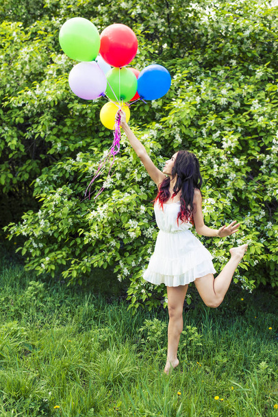 Portrait of young girl holding colorful balloons against blooming apple trees - Photo, Image