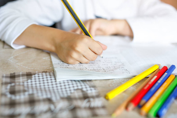 Child doing homework and writing story essay. Elementary or primary school class. Closeup of hands and colorful pencils - Foto, imagen