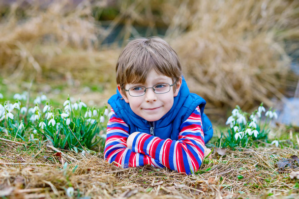 Aranyos szőke óvodáskorú gyerek fiú felfedezése az első tavaszi virágok, szép hóvirág - Fotó, kép