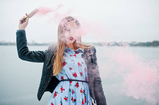 Stylish girl in leather jacket hold pink smoke flare at winter d - Photo, image