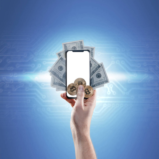 Рука держит мобильный телефон с пустым экраном и биткойнами, долларовые купюры на синем фоне. Цифровой мониторинг, проверка и обмен валюты
 - Фото, изображение