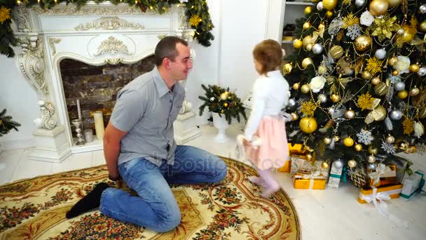 Young Adult Dad With Little Daughter Exchange Gifts and Hugging Each Other in Large Room on Background of Decorated Fireplace and Christmas Tree. - Footage, Video
